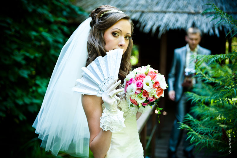 Фото невесты с букетом и веером в фокусе, а жениха — в расфокусе