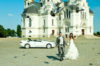 Жених с невестой гуляют по площади. Вдали стоит свадебный лимузин-кабриолет. Над ними кружатся голуби