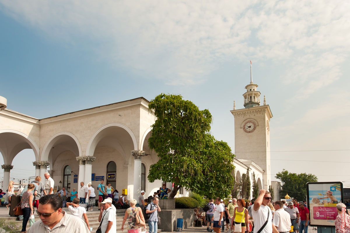 Фото железнодорожного вокзала Симферополя летом, видны арки и вокзальная башня с часами