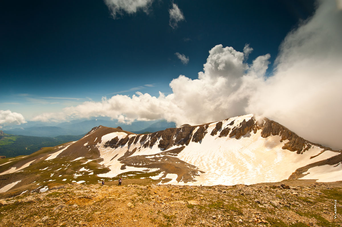 Фото одного из скалистых гребней горы Оштен, справа — густые белые облака на фоне синего неба