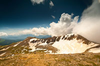 Красивый вид на один из скалистых гребней горы Оштен. Справа — густые белые облака на фоне синего неба