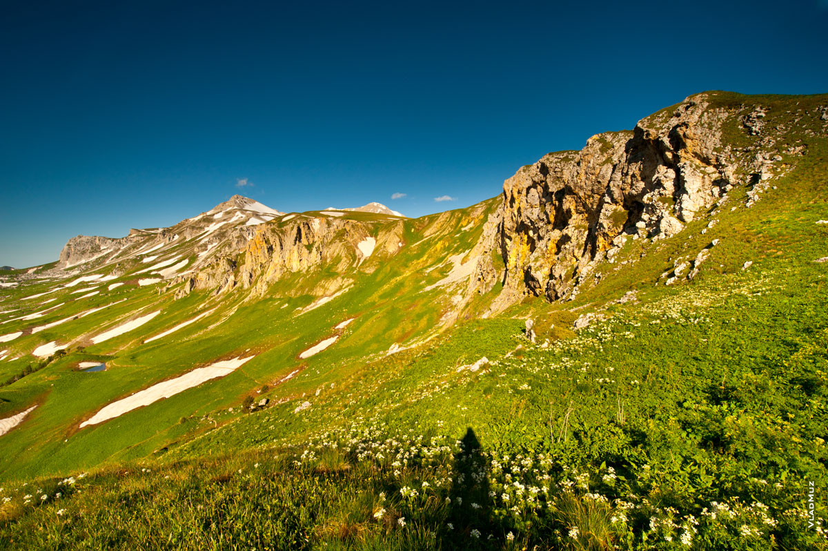 Горный фото пейзаж: травянистые горные склоны внизу, вверху справа скалистые гребни, слева гора Оштен