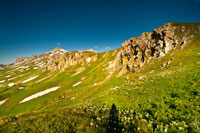 Горный фото пейзаж: травянистые горные склоны внизу, вверху справа скалистые гребни, слева видна гора Оштен