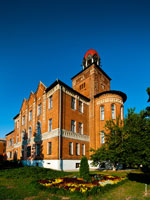 Фото здания учебного корпуса №2 из красного кирпича на фоне синего неба и клумбы перед ним