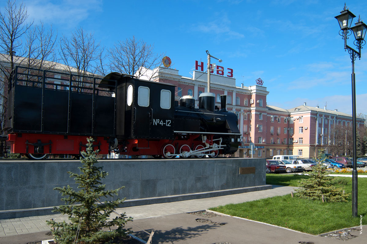 Фото памятника паровозу в Новочеркасске с видом на здание заводоуправления НЭВЗа