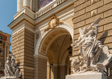 Фото герба Одессы над арочным сводом и скульптур, олицетворяющих комедию (справа) и трагедию (вдали, слева), на входе в Одесский театр оперы и балета