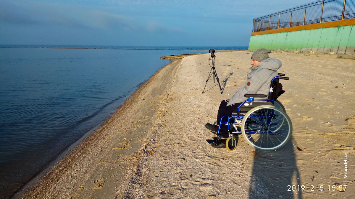 Фото мужчины в инвалидной коляске на пустынном песчаном берегу в районе бухты-заводи для кайтсёрфинга