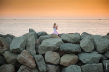 Фото девушки с телефоном на каменистой набережной Имеретинского морского порта, снимающей закат